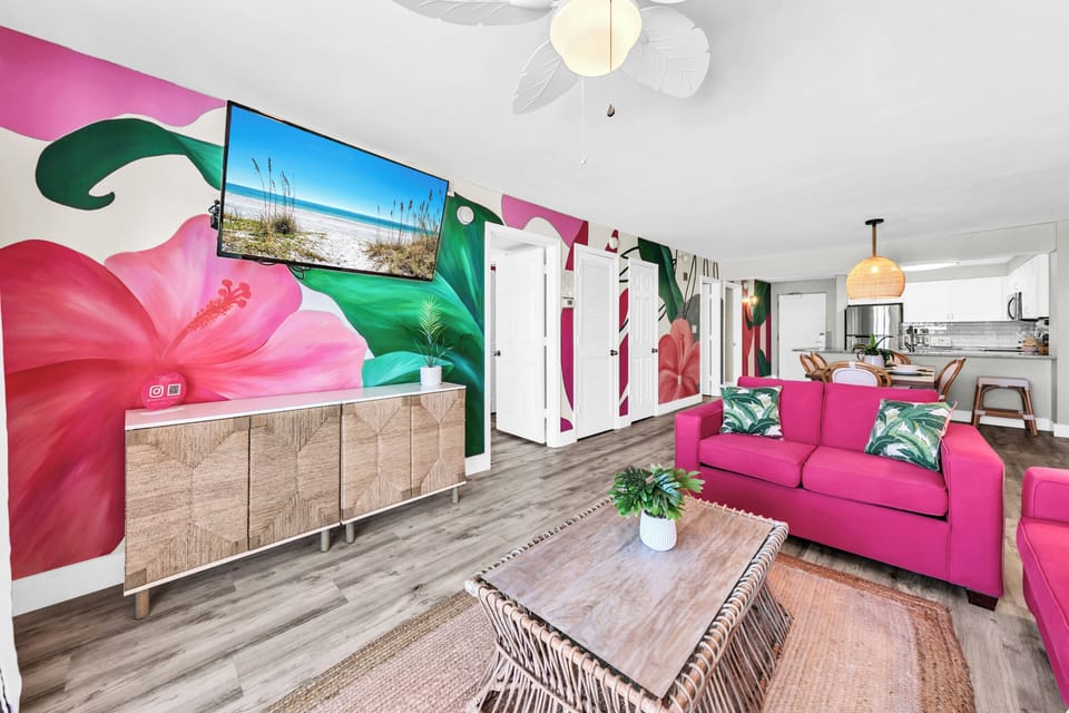 Relax in your vibrant tropical paradise with stunning floral murals, plush pink seating, and modern entertainment setup.