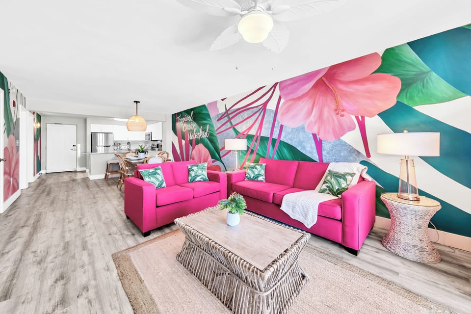 Unwind in your vibrant tropical oasis featuring bold pink sectional seating and stunning botanical murals that create an energizing, colorful retreat.