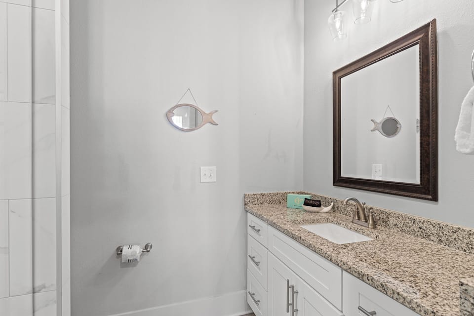 Your private bathroom features granite countertops, crisp white cabinetry, and thoughtful coastal touches that create a serene morning routine.