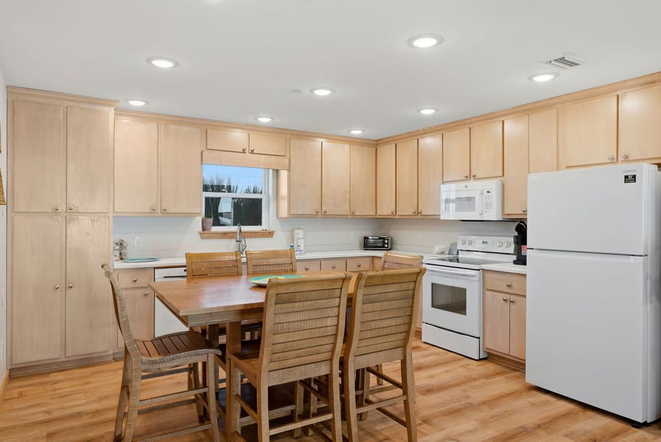 Your spacious kitchen features warm wood cabinetry, modern white appliances, and a welcoming dining table—perfect for gathering with loved ones over home-cooked meals.