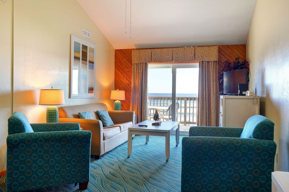 This inviting living space features comfortable seating, coastal decor, and sliding glass doors that open to a private balcony overlooking the ocean.