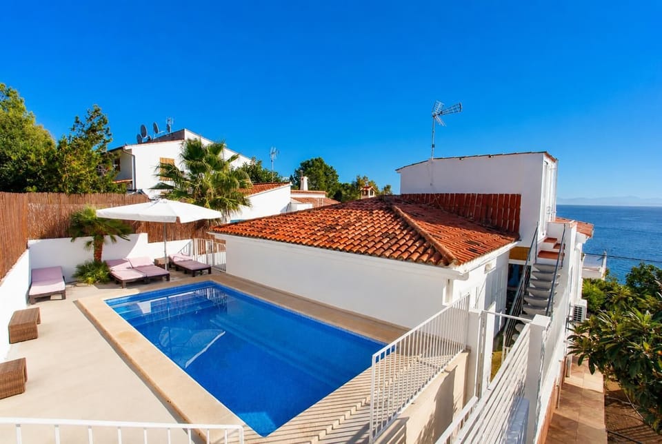 A private swimming pool and sun terrace sit alongside a terracotta-tiled roof, offering coastal views of the sea under a clear blue sky.