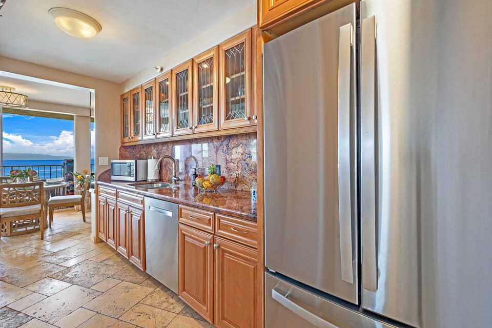 Modern kitchen with stainless appliances and ocean view, sunlight glinting off countertops while sea breezes drift through the open door.