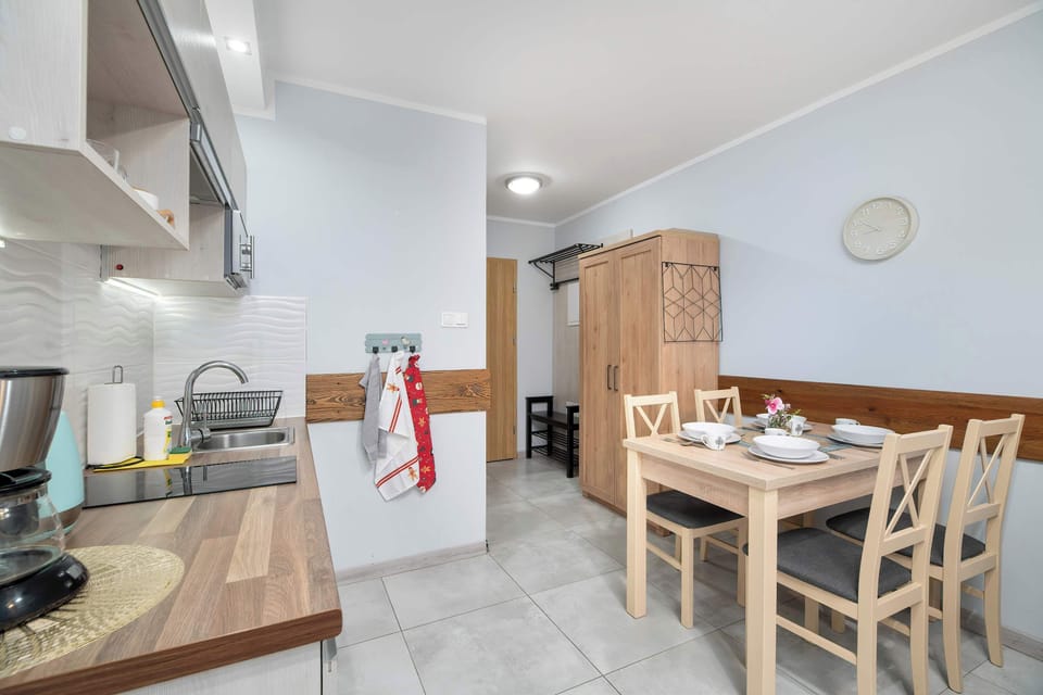 A kitchen and dining space with a small table and modern appliances. The white and wood color scheme gives it a clean, minimalist look.