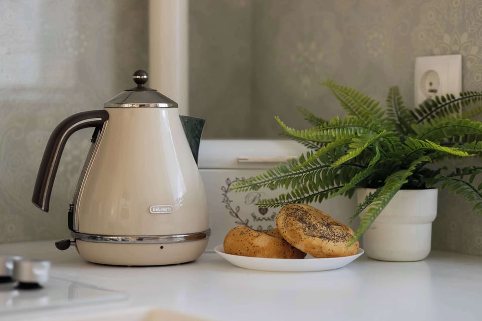 A detailed shot focuses on a stylish beige electric kettle and a potted fern on a white kitchen countertop. This adds a touch of homeliness and focus on small details.