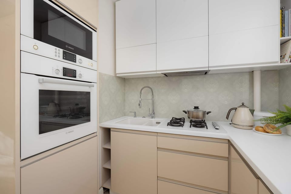 The modern kitchen is showcased, featuring sleek, light beige handleless cabinets and a light countertop. A built-in oven and microwave are integrated into the cabinetry.