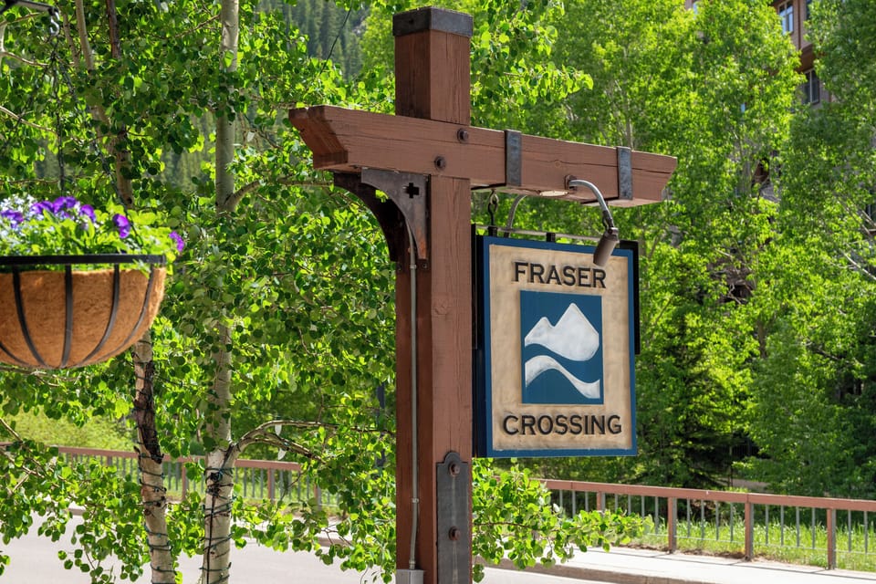 Fraser Crossing property entrance sign nestled among lush green trees and seasonal blooms, marking your arrival at this mountain destination.
