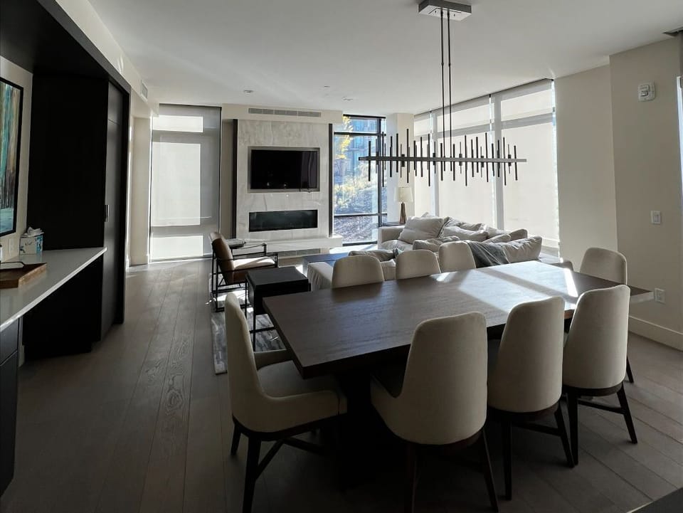 The spacious living area features a modern fireplace, a stylish dining table, and large windows that fill the space with natural light.