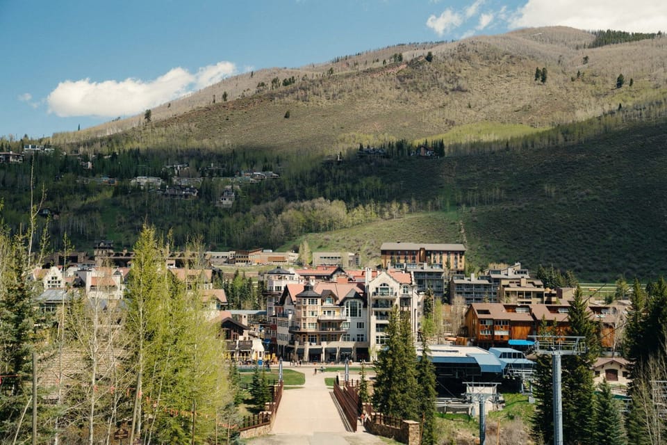 Red-roofed village buildings cluster at the base of a green mountain slope in summer