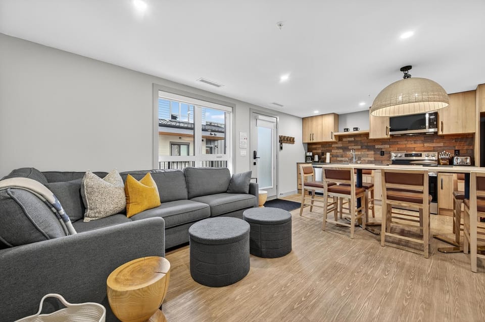 The open layout of the living and kitchen area fosters a relaxed atmosphere, with natural light pouring in through large windows that frame the outdoor scenery while stylish furnishings enhance the homey feel.