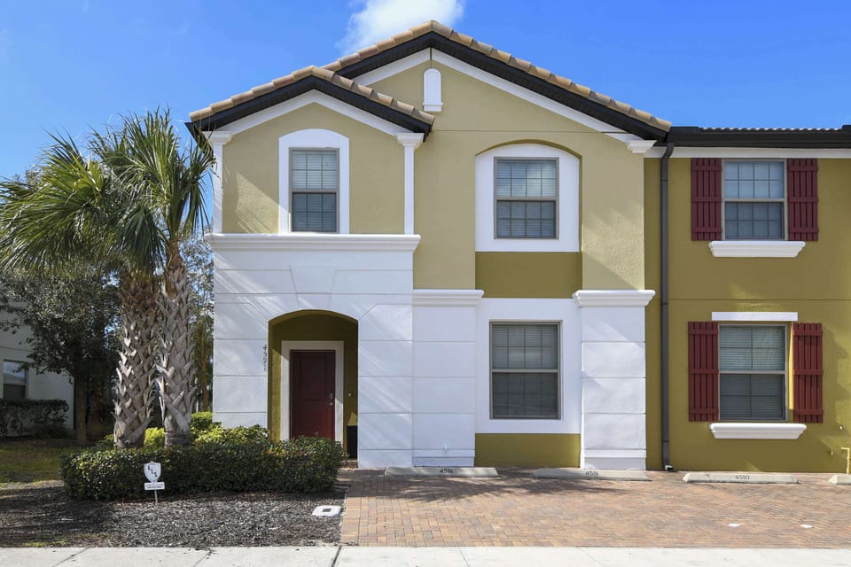 Exterior view of a modern townhouse with a tiled roof and palm trees.