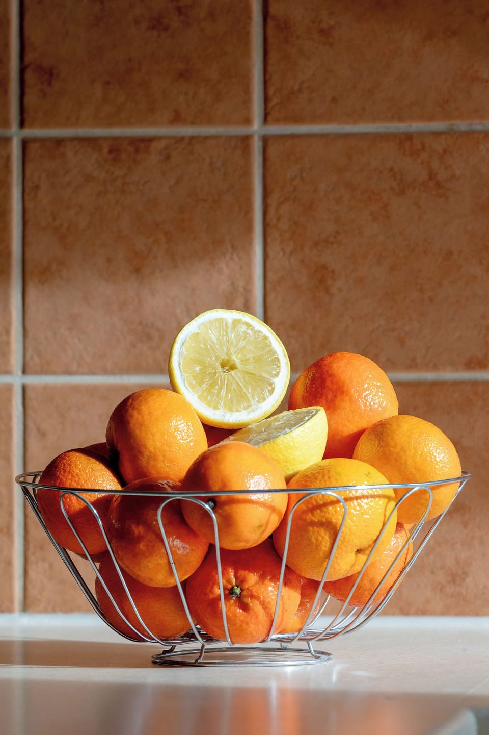A bowl of oranges with a slice of lemon on top, placed on a kitchen counter.