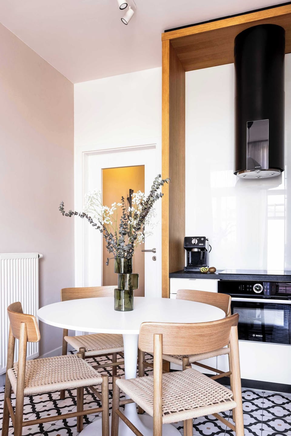 Cozy dining area set next to the modern kitchen, featuring a round table and natural wooden chairs. The bright, minimalist design creates a pleasant spot for meals or morning coffee.