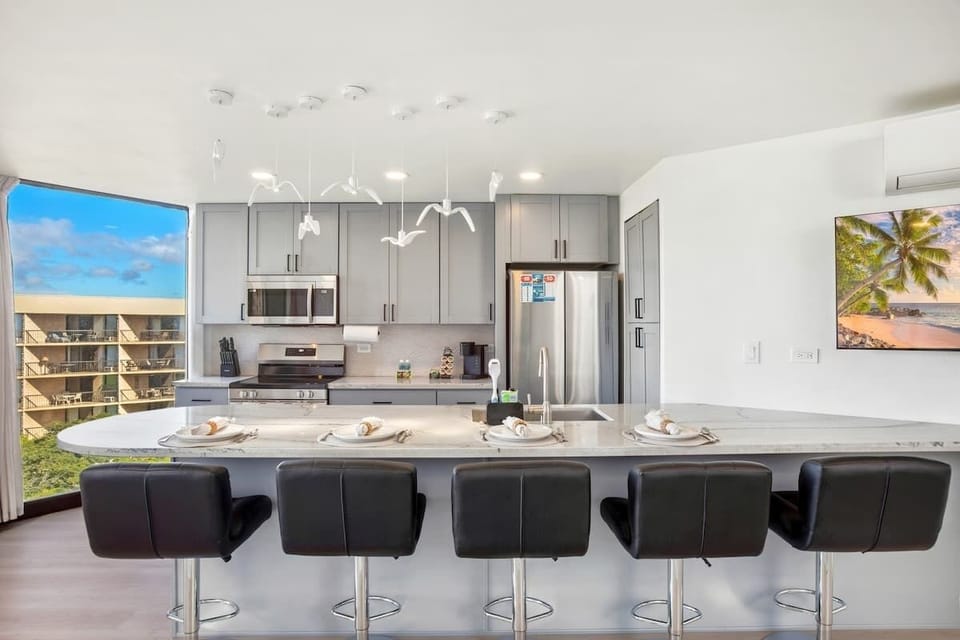 Gather around the sleek, curved kitchen bar with seating for five, offering a full view of the modern, fully-equipped kitchen and a captivating view through the floor-to-ceiling window.