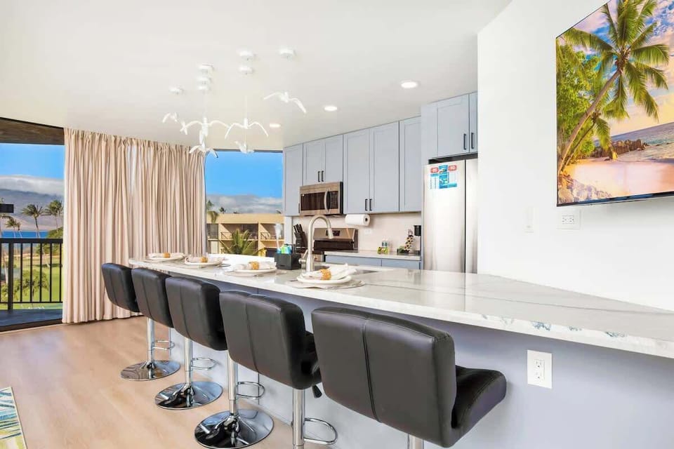 Dine with a stunning ocean view at the kitchen island, featuring modern black bar stools, a marble countertop, and unique seagull light fixtures.