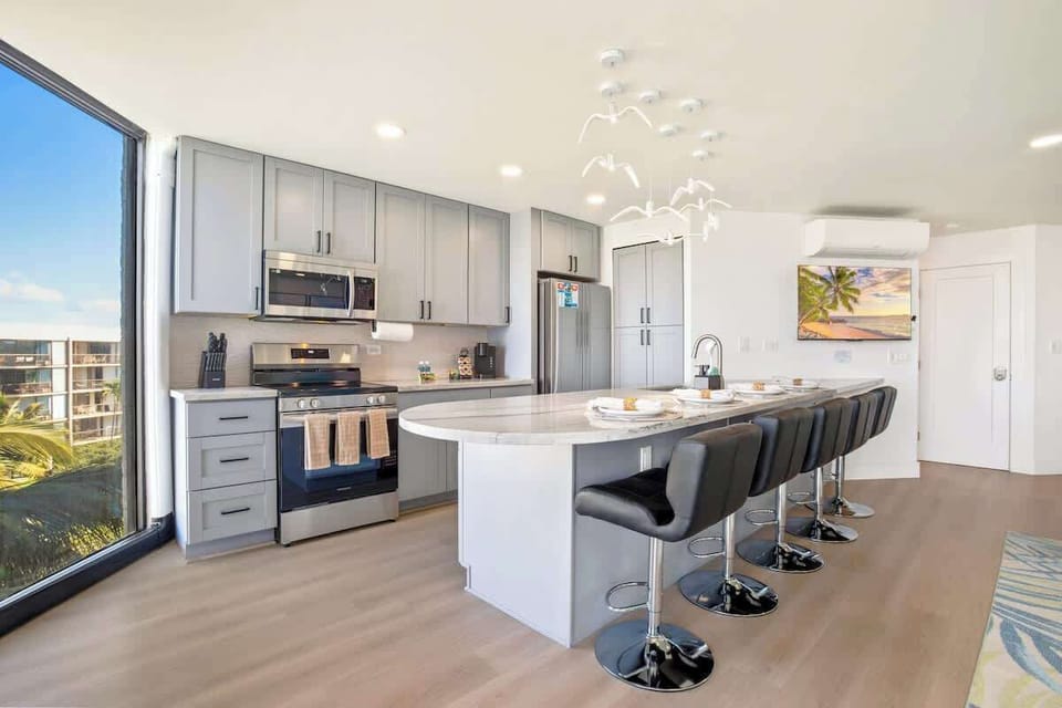 This chic kitchen features sleek gray cabinets, stainless steel appliances, and a curved bar seating area with captivating views through the large window.
