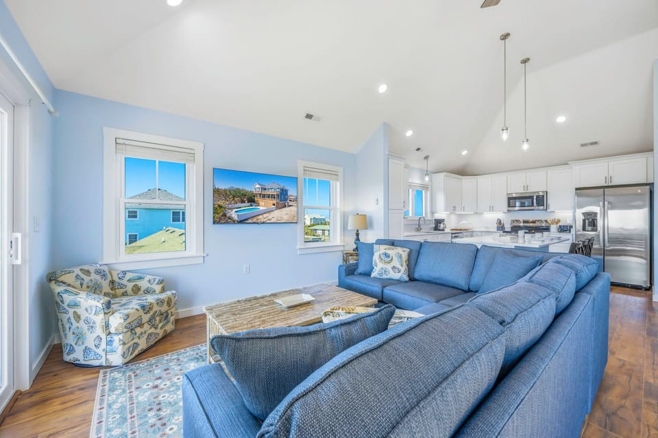 Relax in your spacious living area with plush blue sectional seating and ocean-inspired décor, seamlessly connected to a modern kitchen.