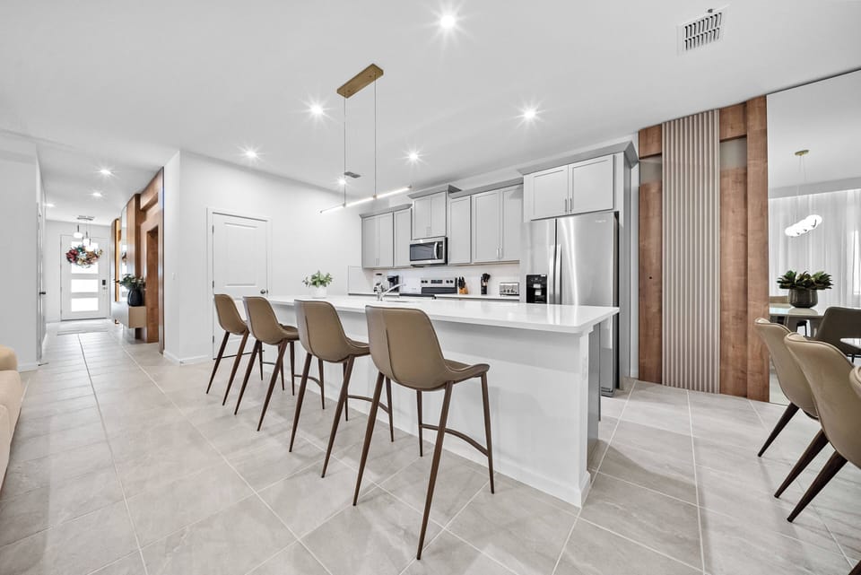 Enjoy a bright kitchen with sleek white cabinetry and a spacious island with stylish bar stools for casual dining. Warm wood accents add charm, and modern appliances provide convenience for a delightful stay.