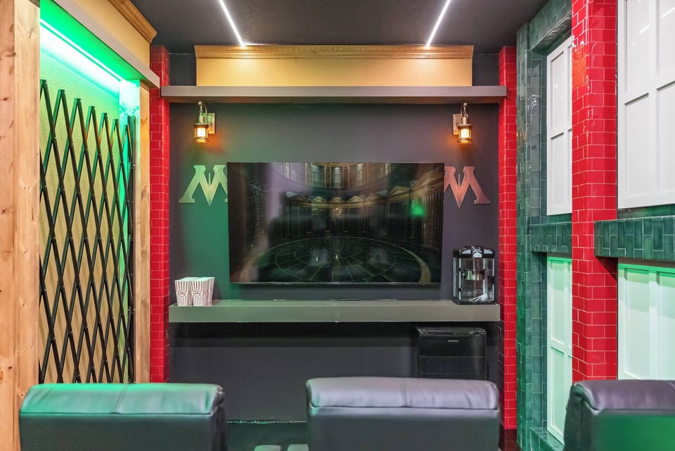 Discover a chic entertainment area featuring sleek black leather seating and lively red and green accents. The wall-mounted TV and warm hanging lights create a cozy atmosphere ideal for movie nights or game days.