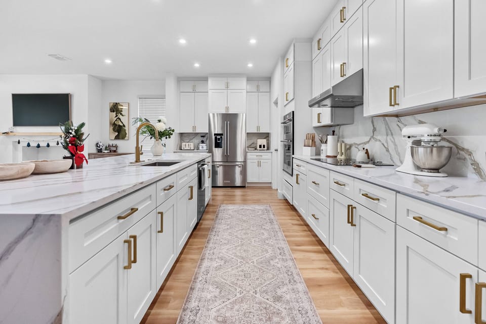 Experience a stunning kitchen with sleek white cabinetry and elegant gold accents. The spacious layout offers a large marble countertop ideal for meal prep, while soft lighting creates a warm and inviting atmosphere for cooking.