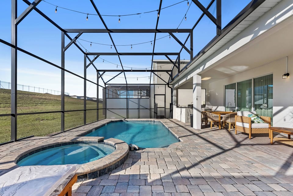Step outside to a beautifully designed outdoor space with a sparkling pool and relaxing spa, surrounded by charming paver stones. Enjoy comfortable seating under soft string lights, perfect for unwinding and evening chats.