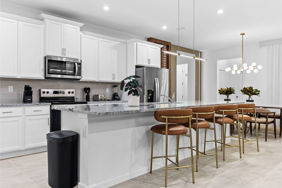 Experience a stylish kitchen with elegant white cabinetry and a stunning granite countertop, accented by warm gold bar stools. The open design flows effortlessly into the dining area, brightened by a chic pendant light.