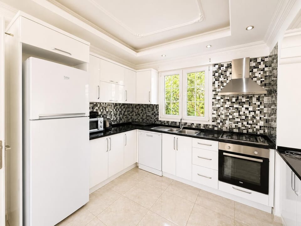 Modern white kitchen with black worktops, mosaic backsplash, and fully equipped appliances.