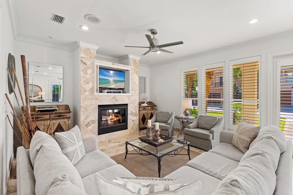 Unwind in your elegant living space with plush seating, warm fireplace, and peaceful garden views through plantation shutters.