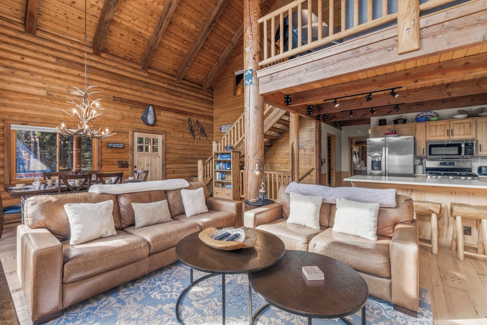 Features a wall of floor to ceiling windows, cozy leather couches centered around a Smart TV, and a wood-burning stove on a majestic stone hearth
