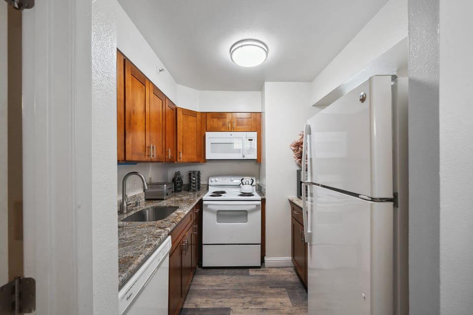 Galley kitchen with granite counters and warm wood cabinetry, fully equipped for easy vacation cooking.