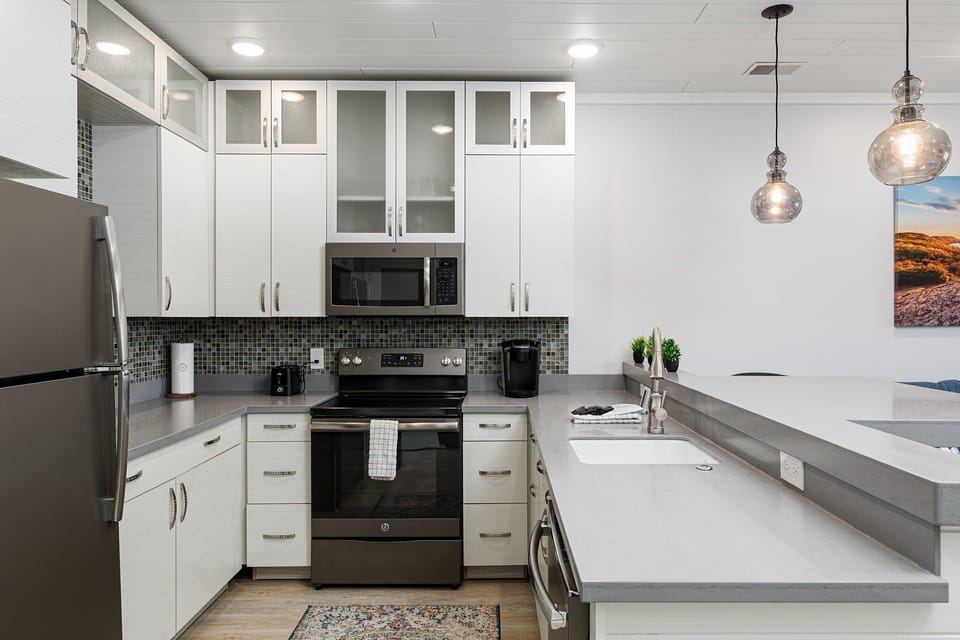 Bright kitchen w/ peninsula seating, pendant lighting & stainless steel appliances.