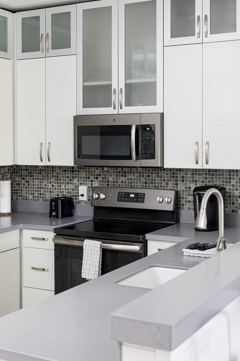 Stainless steel range & microwave paired w/ mosaic tile backsplash for a polished finish.