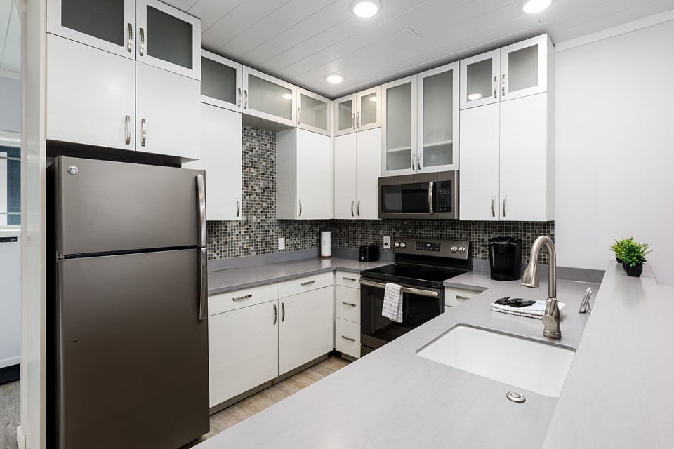 Sleek kitchen w/ white cabinetry, stainless steel appliances & mosaic backsplash for easy meals.
