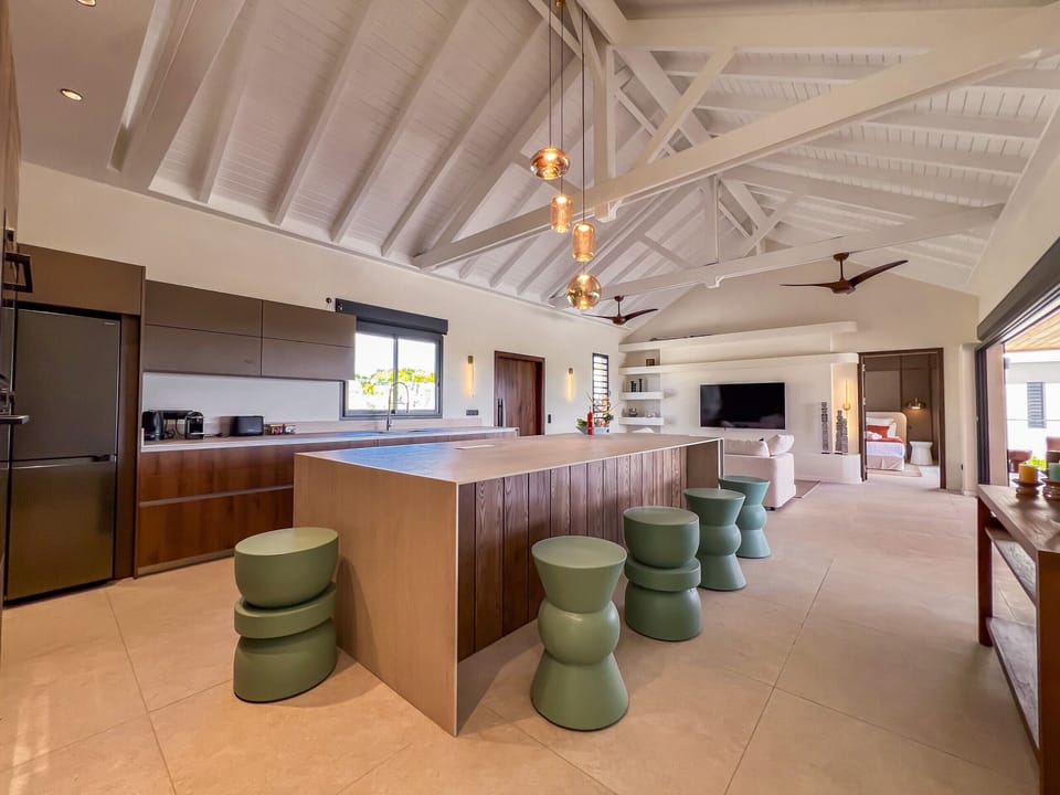This modern open-plan kitchen combines natural materials and contemporary design. The spacious wooden island, elegant pendant lights and vaulted ceiling create a warm, inviting atmosphere. The layout flows seamlessly into a bright living area, perfect for relaxing and entertaining.