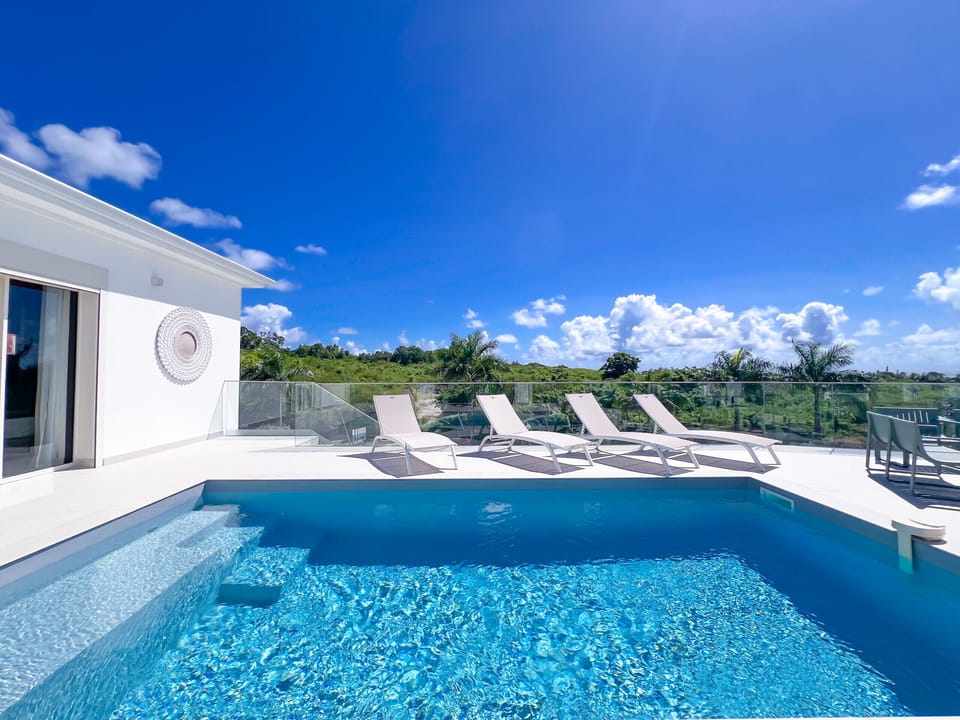 A bright, contemporary terrace featuring a crystal-clear turquoise pool and several sun loungers overlooking lush greenery. The perfect spot to relax, unwind, and enjoy a premium outdoor living experience.