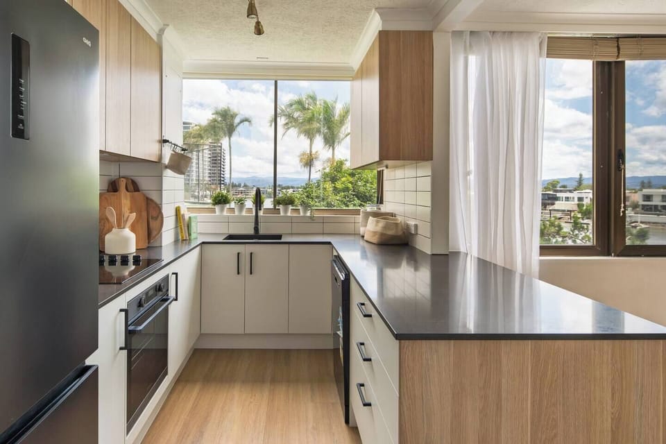 A bright, fully equipped kitchen offers modern appliances, generous bench space, and lush palm-lined views, making everyday cooking effortless and enjoyable.