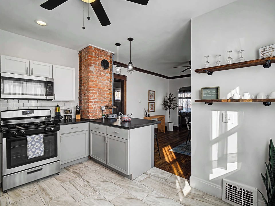 Bright kitchen w/ white cabinets, open shelving & brick accent wall
