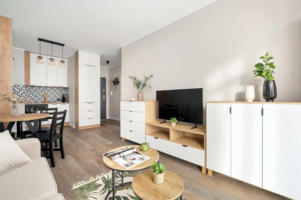 A bright living area with a sofa, modern furniture, and a mounted TV. Decorative plants and neutral tones create a calm, welcoming ambiance.