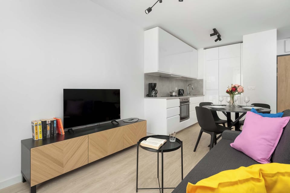 Living room corner featuring a grey sofa with colorful pillows and a wooden TV stand.