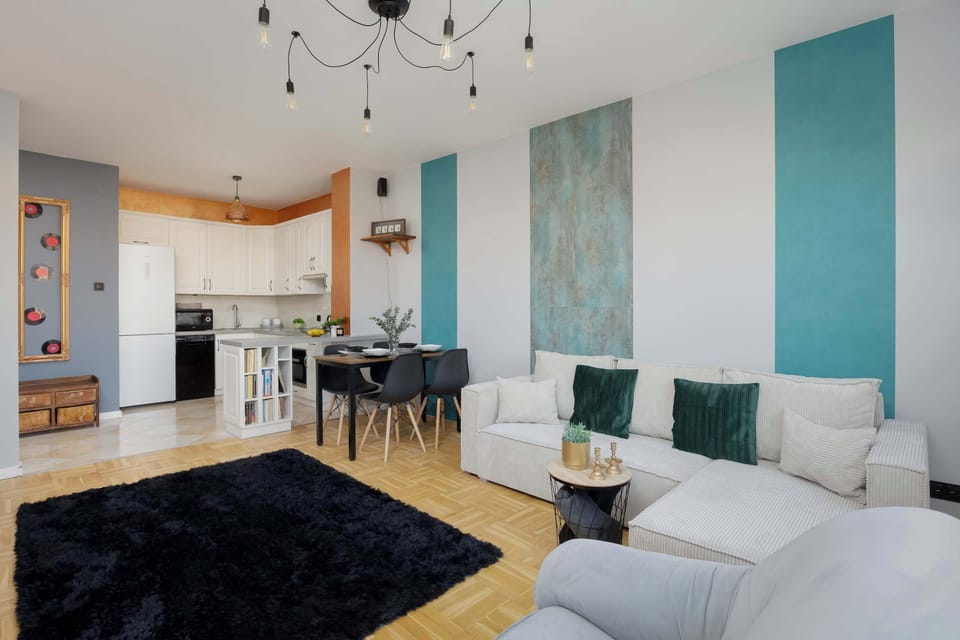 An open living-and-dining area featuring a sectional sofa and a kitchen in the background. The modern chandelier adds elegance to the space.