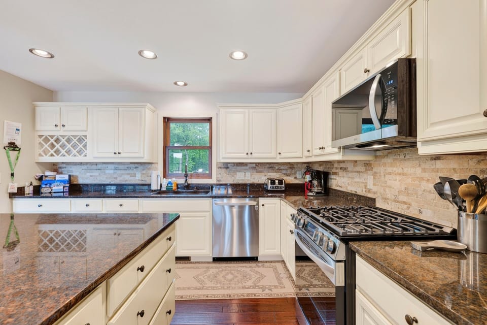 A large white kitchen with dark wood floors with a stainless steel dishwasher and  large gas stove with a microwave above it.