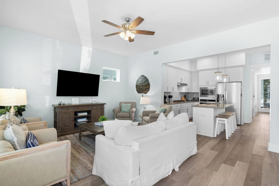 Open concept living room with a large sofa, area rug, mounted television, and ceiling fan.