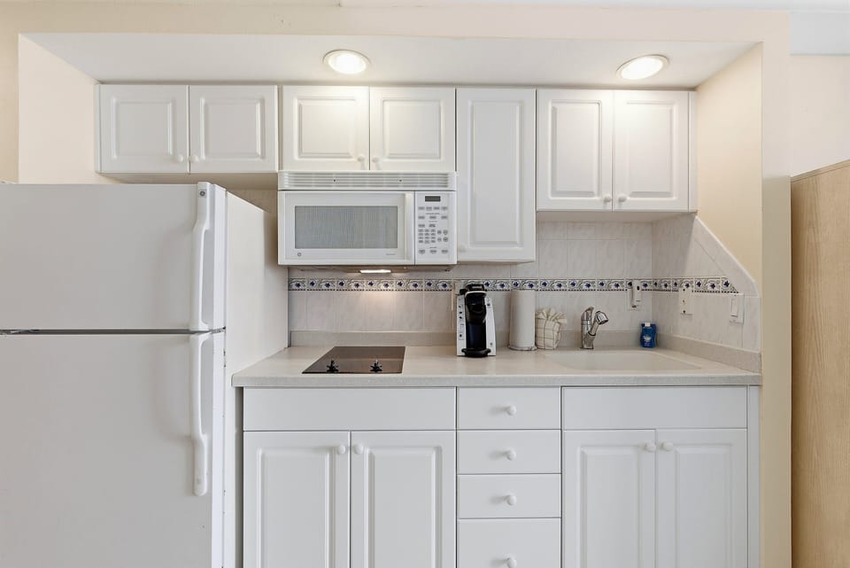 Prepare snacks, quick meals, and morning coffee with ease in this convenient kitchenette featuring a refrigerator, microwave, cooktop, sink, and Keurig. A perfect addition to a comfortable and carefree beach stay.