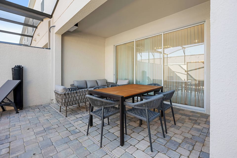 Step outside to enjoy a cozy patio with a sturdy wooden dining table and stylish, weather-resistant chairs. The smooth stone pavers and natural light make it a perfect spot for al fresco dining or morning coffee.