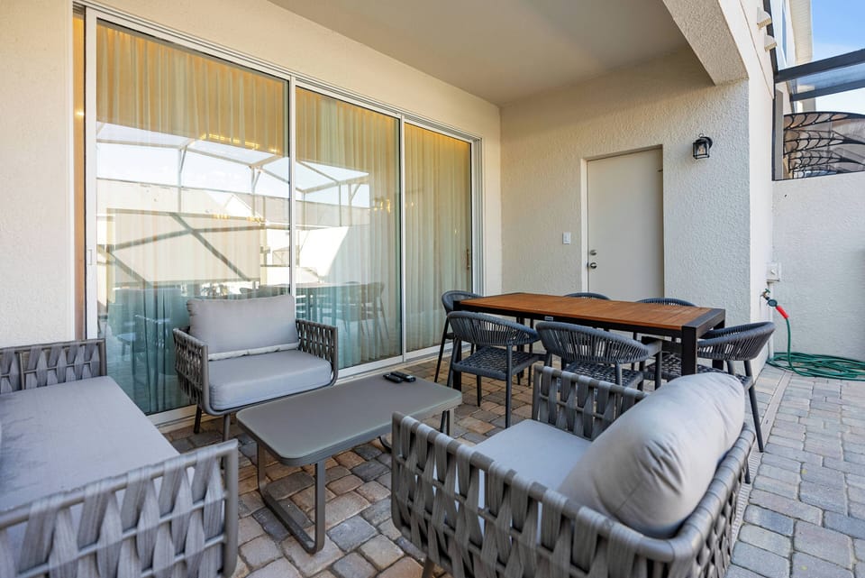 Step outside to a charming patio with stylish woven furniture perfect for relaxation. The cozy gray cushions complement the warm stone flooring, and large glass doors create a seamless flow between indoor and outdoor spaces.