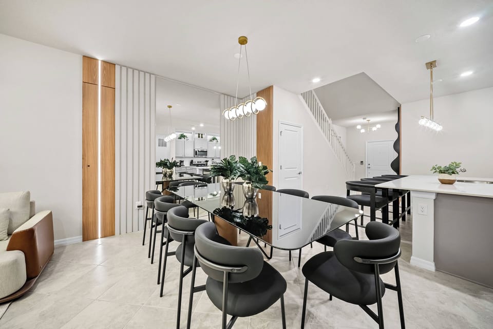 Join us at our sleek glass dining table, where stylish black chairs invite conversation. The bright, airy space, with warm wooden accents and modern lighting, offers a welcoming atmosphere perfect for meals and gatherings.