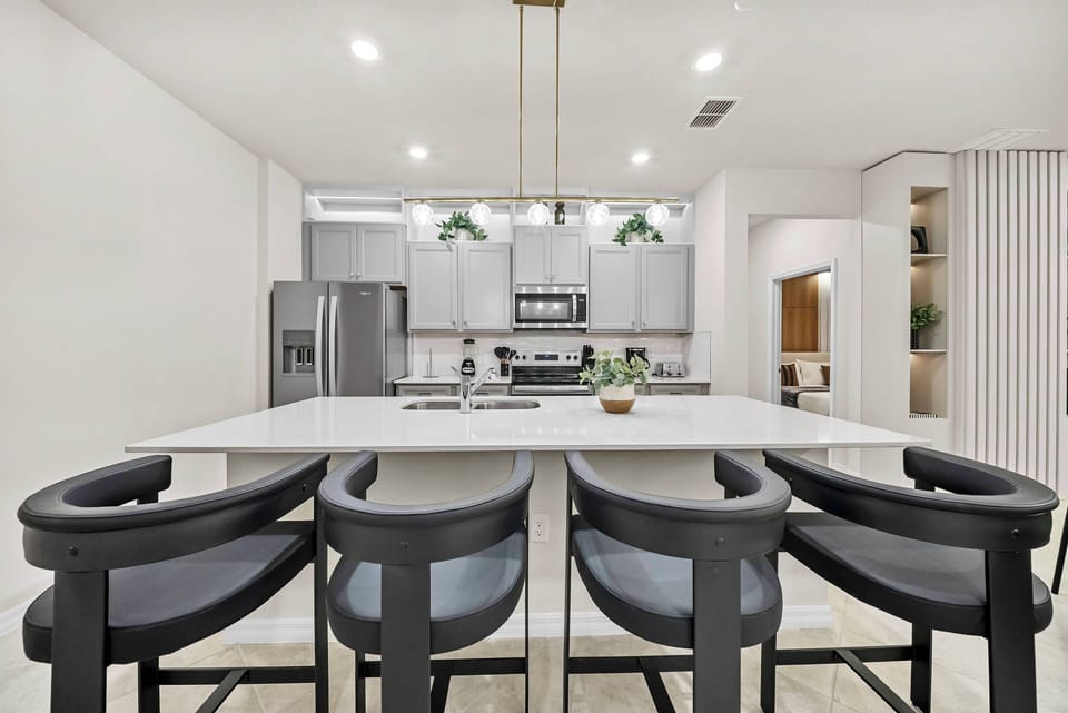 This stylish kitchen boasts a spacious island with chic black bar stools ideal for casual dining or morning coffee. The modern cabinetry and stainless steel appliances create a bright, inviting space for your culinary adventures.