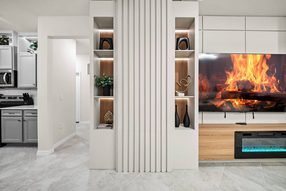 Experience a cozy living area with a sleek entertainment center and a warm electric fireplace for added comfort. Tasteful decor and greenery on the built-in shelves create a perfect blend of style and relaxation for your stay.