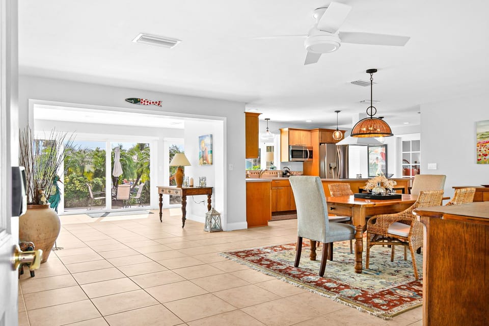 Step into your tropical retreat where warm wood tones and island breezes create the perfect backdrop for memorable meals. The open kitchen flows seamlessly into your dining space, while lush garden views through oversized windows remind you that paradise i