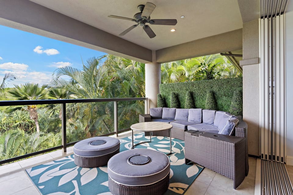 A shaded outdoor lounge featuring a sectional sofa and ottomans, perfect for relaxing with tropical views